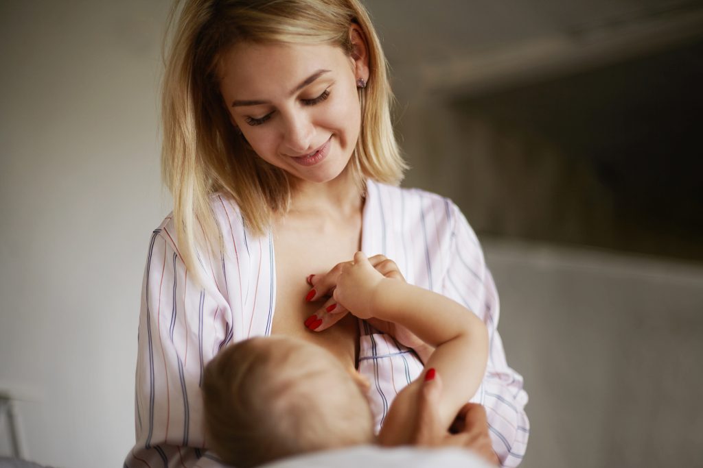 back view of adorable six month old infant drinking breast milk attractive young european woman in home clothing cradling her baby daughter in arms breastfeeding her enjoying deep connection