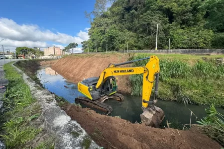 quipe da Prefeitura de Ribeirão Pires realizando desassoreamento no Ribeirão Grande com escavadeiras e equipamentos especializados para prevenção de enchentes.