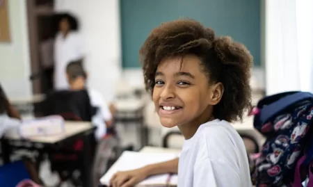 Estudantes em sala de aula de escola pública brasileira, com materiais escolares sobre as carteiras