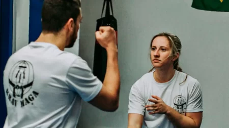 Mulheres participam de aula de Krav Maga, praticando técnicas de defesa pessoal contra agressões.