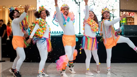 Foliões curtindo o Carnaval em shopping de São Paulo, com decoração colorida e espaço instagramável.