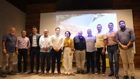 Autoridades e diretores da Braskem posam em um ambiente interno, diante de um telão com a imagem de uma estrutura industrial ou projeto técnico. O local tem iluminação aconchegante, e os participantes estão vestidos de maneira formal e semiforma, sugerindo um evento corporativo ou técnico.